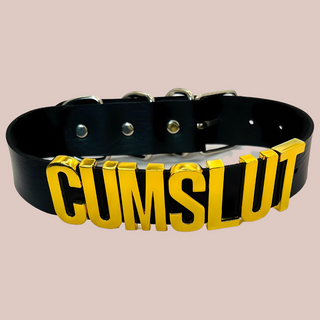 A close up view of the Cumslut collar, you can see the gold shiny lettering that is all in capital letters. There is matching silver buckles at the back.