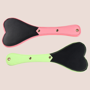 This image of the Luminous Spanking paddles shows the green and pink paddles on offer, you can see the heart shaped head and narrow handle.