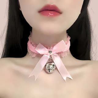 A satin and gauze fabric choker / necklace that has a matching satin bow to the front, with a large hanging bell. There are ribbon string ties to the back, allowing for different sized necks and it comes in soft pink.