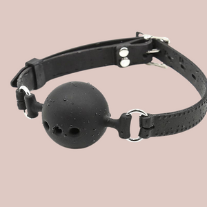 The black silicone lockable ball gag, you can see the ball with air holes and the strap that wraps around the head.