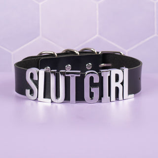 A close up of the Slut Girl Collar, it has a black collar and silver lettering.